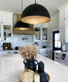 a large kitchen with white cabinets and black pendant lights above the island countertop, along with two vases filled with dried flowers