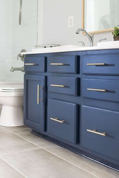 a white toilet sitting next to a blue vanity in a bathroom under a large mirror