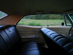 the interior of an old car with black leather seats and a field in the background