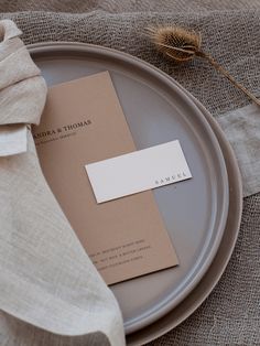 a plate with a place card on it next to a napkin and some dried flowers