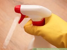 a hand in yellow rubber gloves holding a spray bottle with red and white trigger marks on it