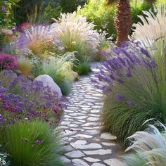 a stone path surrounded by purple and white flowers in the middle of a garden with palm trees