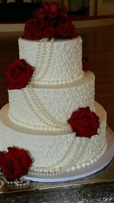 a three tiered wedding cake with red roses on the top and pearls on the bottom