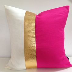 a pink and white pillow with gold stripes on the side, sitting on a table