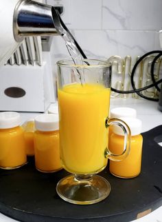 an orange juice being poured into a glass on top of a kitchen counter next to jars