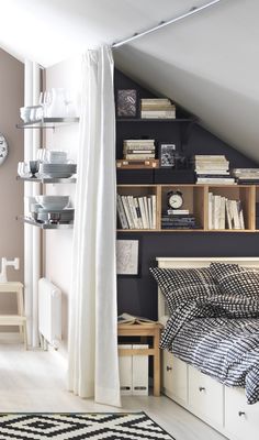 a bed sitting under a window next to a shelf filled with books and other items