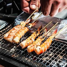 someone is cooking shrimp on the grill with chopsticks in their hand and another person's hand reaching for it