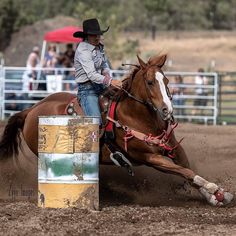 a man riding on the back of a brown horse next to a barrel in an arena