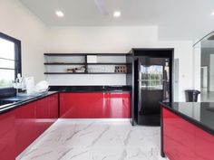 a large kitchen with red cabinets and black counter tops, along with white marble flooring