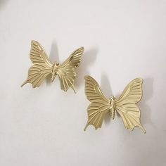 two gold colored butterfly shaped earrings sitting on top of a white table next to each other