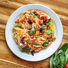 a plate of pasta with tomatoes, olives and spinach on a wooden table