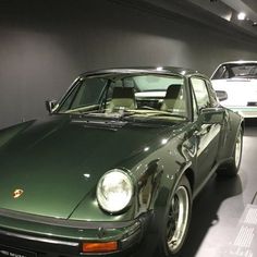 two porsches are on display in a showroom, one is green and the other is white