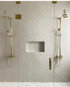 a walk in shower sitting next to a white tiled wall with gold fixtures on it