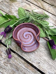 a ceramic bowl with purple flowers and green leaves on a wooden table next to it