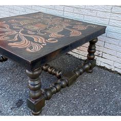 an old wooden table with decorative paint on it's top and legs, sitting in front of a brick wall