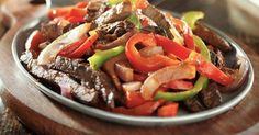 a plate full of beef and peppers on top of a wooden cutting board with a spoon