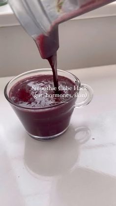 a person pouring red liquid into a glass bowl on top of a white countertop