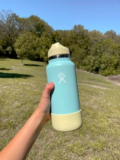 a hand is holding a blue and yellow water bottle in the grass with trees in the background