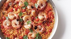 a skillet filled with pasta and shrimp, garnished with fresh basil leaves