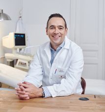 a man sitting at a table in front of a dentist's chair smiling for the camera