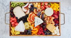 a wooden tray filled with assorted fruits and cheese on top of a marble counter