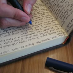 a person writing on an open book with a pen in their left hand and a small blue ballpoint pen next to it