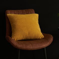 a brown chair with a yellow pillow sitting on top of it next to a potted plant