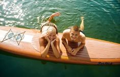 two people are laying on a surfboard in the water with their hands behind their heads