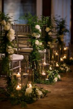 an aisle with candles, flowers and greenery on the side is decorated with glass vases