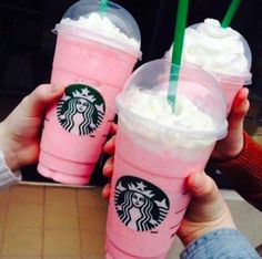 two people holding up starbucks drinks with straws in their hands and one is pink