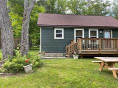 there is a picnic table in the yard next to a small gray house with a porch