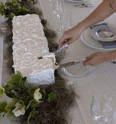 a person cutting into a cake on top of a table with flowers and greenery