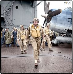 black and white photograph of men walking on the deck of an aircraft carrier while other people watch