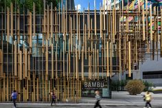 people walking on the sidewalk in front of a building with wooden slats covering it