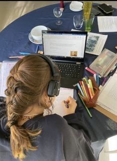 a woman sitting at a table with headphones on her ears and writing in a notebook