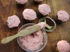 cupcakes with pink frosting and a wooden spoon on a table next to them