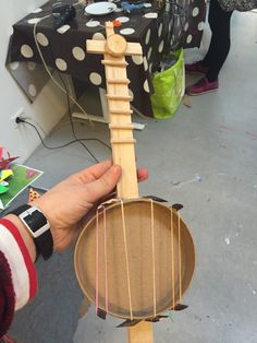 a person holding a small wooden instrument in their left hand with strings attached to it