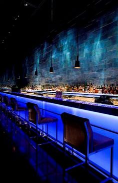 an empty bar is lit up with blue lights and black chairs in front of the bar