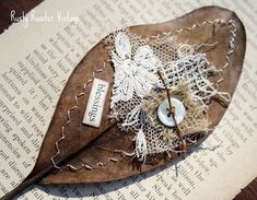 an old leaf with lace and buttons on it sitting on top of a piece of paper