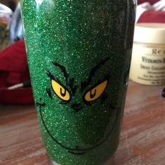 a green cup with yellow eyes on it sitting on top of a wooden table next to other items