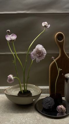 two vases with flowers in them sitting on a table next to rocks and a cup