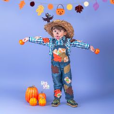 a young boy wearing a cowboy hat and overalls standing in front of pumpkins