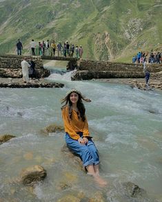 a woman sitting on top of a rock in the middle of a river next to a bridge