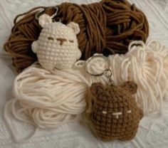 two crocheted items are sitting on a white surface next to yarn and a teddy bear keychain