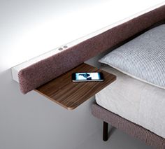 a cell phone sitting on top of a wooden table next to a white bed with pillows