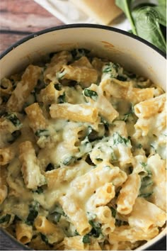 a pot filled with pasta and spinach on top of a wooden table