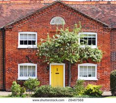 a red brick house with white windows and yellow door in the country side garden area