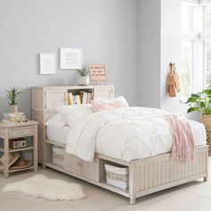 a bed with white sheets and pink pillows in a room next to a potted plant