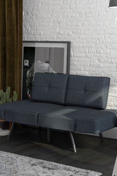 a blue couch sitting in front of a white brick wall next to a potted plant