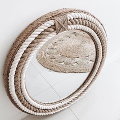 a round mirror sitting on top of a white floor next to a rope covered wall